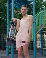 Jason steht in einem pinken Jersey, mit einem Skateboard über dem Arm vor einem Klettergerüst